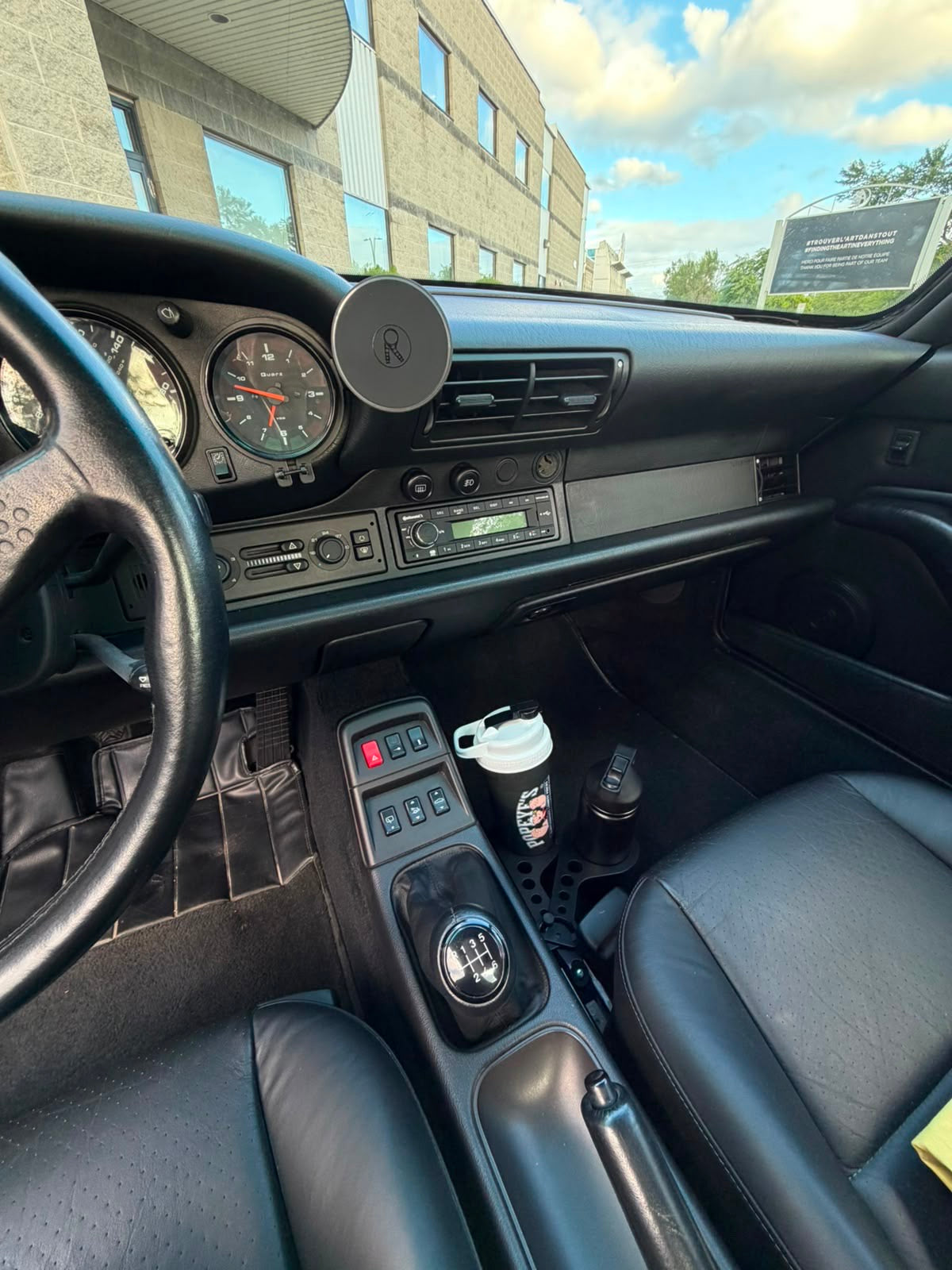Wide Porsche 911 cockpit showing the Rinashi phone mount and seat-rail cup holder